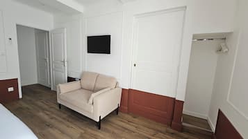 A room with a beige sofa, a flat-screen TV mounted on the wall, and a wooden floor.