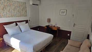A hotel room with a bed, a desk, a chair, and a wooden floor.