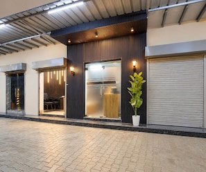 A modern building with a glass entrance, a potted plant, and a closed shutter door. - Deluxe Room Hotel Shreeda (Greater Noida)