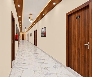 A hotel hallway with marble flooring, wooden doors, and recessed lighting. - Deluxe Room Hotel Shreeda (Greater Noida)