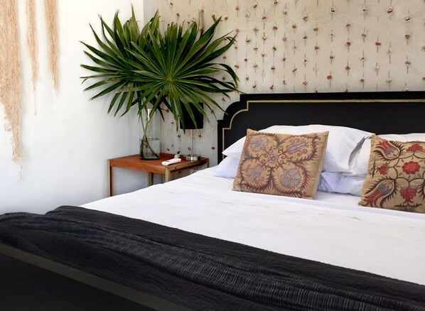 A bed with a black headboard, white bedding, and patterned pillows. There is a large green plant to the left of the bed. - 3-bedroom house with hacienda-inspired kitchen in charming Centro with AC (Centro)