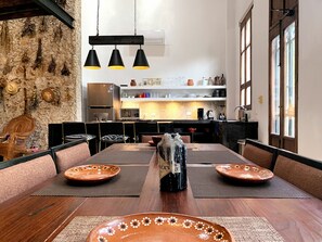 A dining area with a long wooden table, black chairs, and a rustic stone wall. - 3-bedroom house with hacienda-inspired kitchen in charming Centro with AC (Centro)