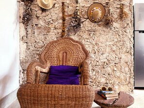 A wicker chair with a purple cushion against a textured stone wall, a hat, and a small table with books and a globe. - 3-bedroom house with hacienda-inspired kitchen in charming Centro with AC (Centro)