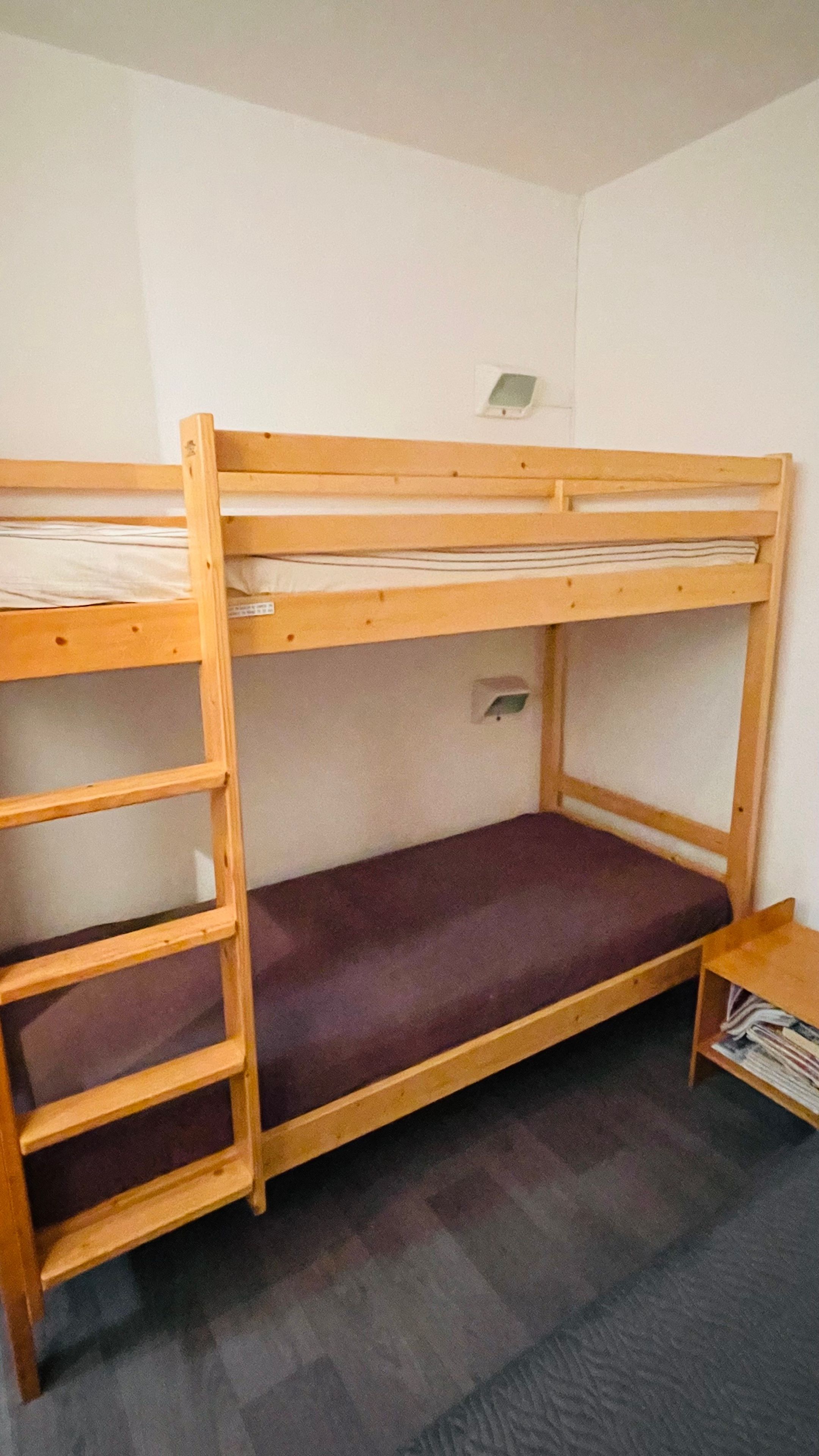 Una cama litera con escalera, un estante pequeño y una lámpara de pared.