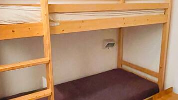 Una cama litera con escalera, un estante pequeño y una lámpara de pared.