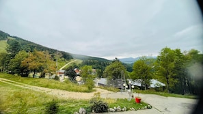 Ländliche Landschaft mit Feldweg, einem kleinen Gebäude und einem bewaldeten Hügel im Hintergrund.
