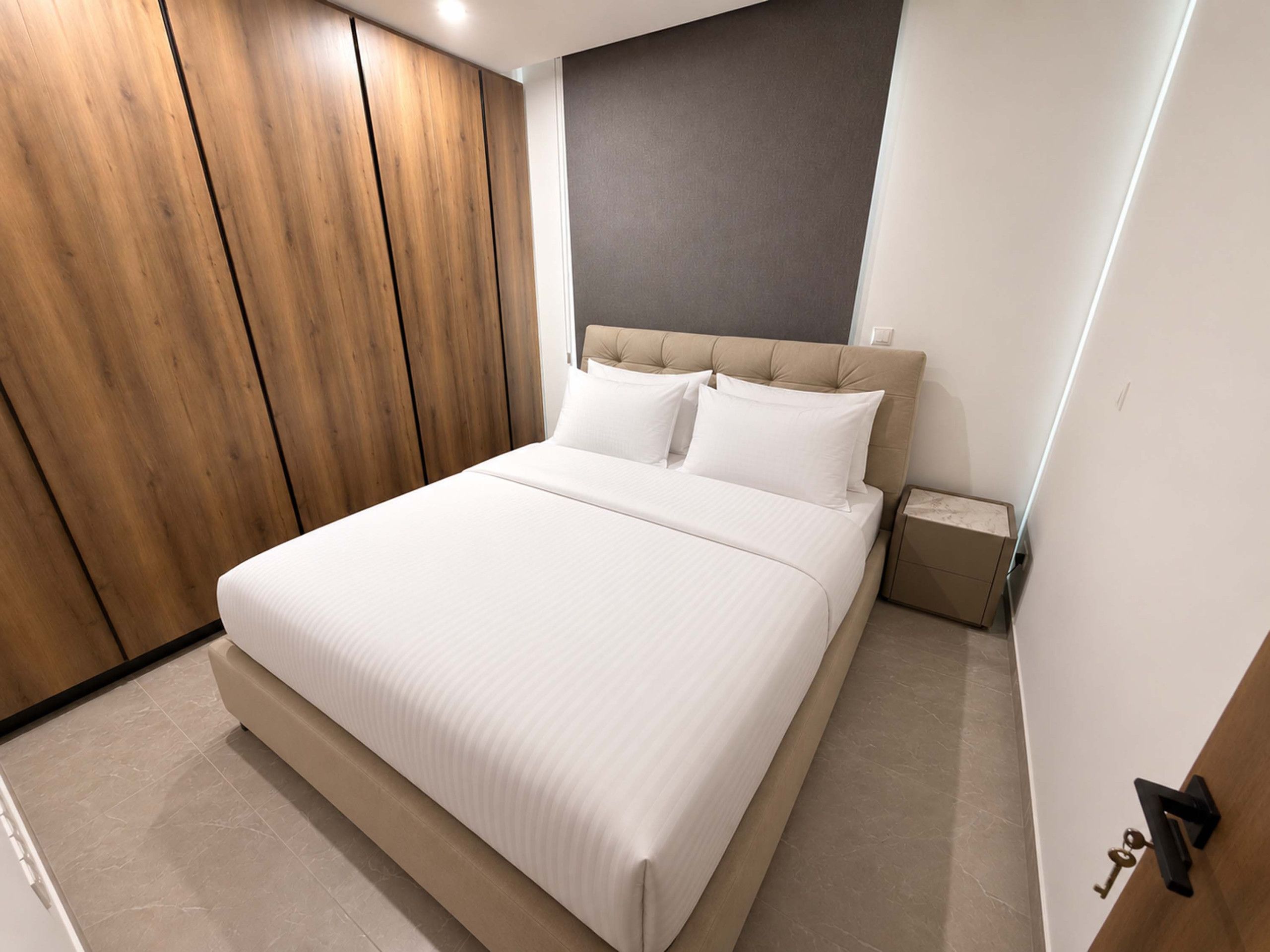 A modern bedroom with a large bed, wooden wardrobe, and a nightstand.