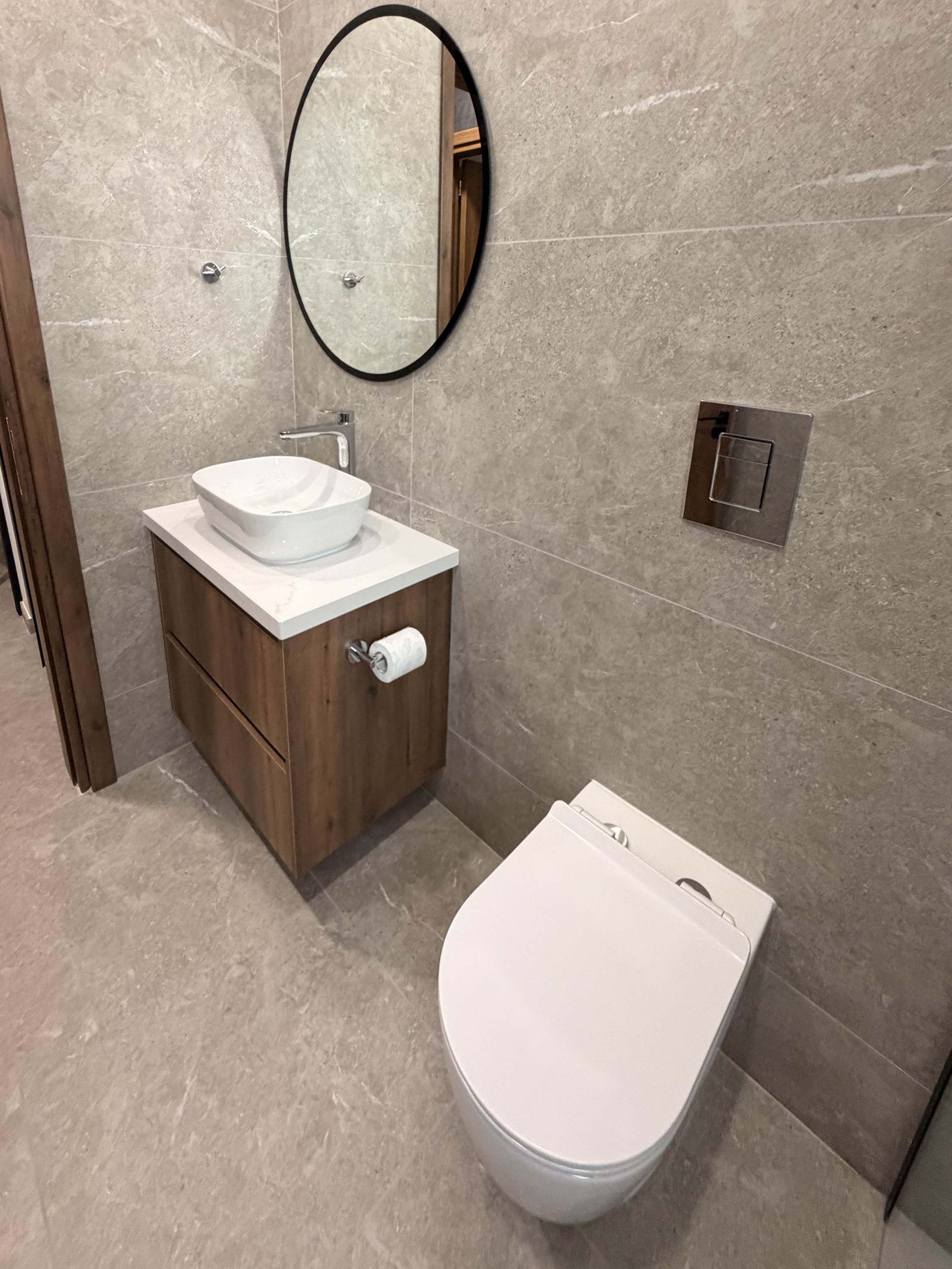 A modern bathroom with a white toilet, a wooden vanity with a white sink, and a round mirror.
