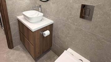 A modern bathroom with a white toilet, a wooden vanity with a white sink, and a round mirror.