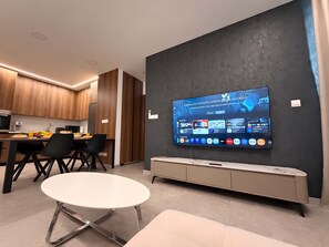 Een moderne keuken met houten kastjes, een eethoek met een witte tafel en stoelen, en een grote flatscreen-tv aan een donkere muur waarop diverse streaming apps worden weergegeven.