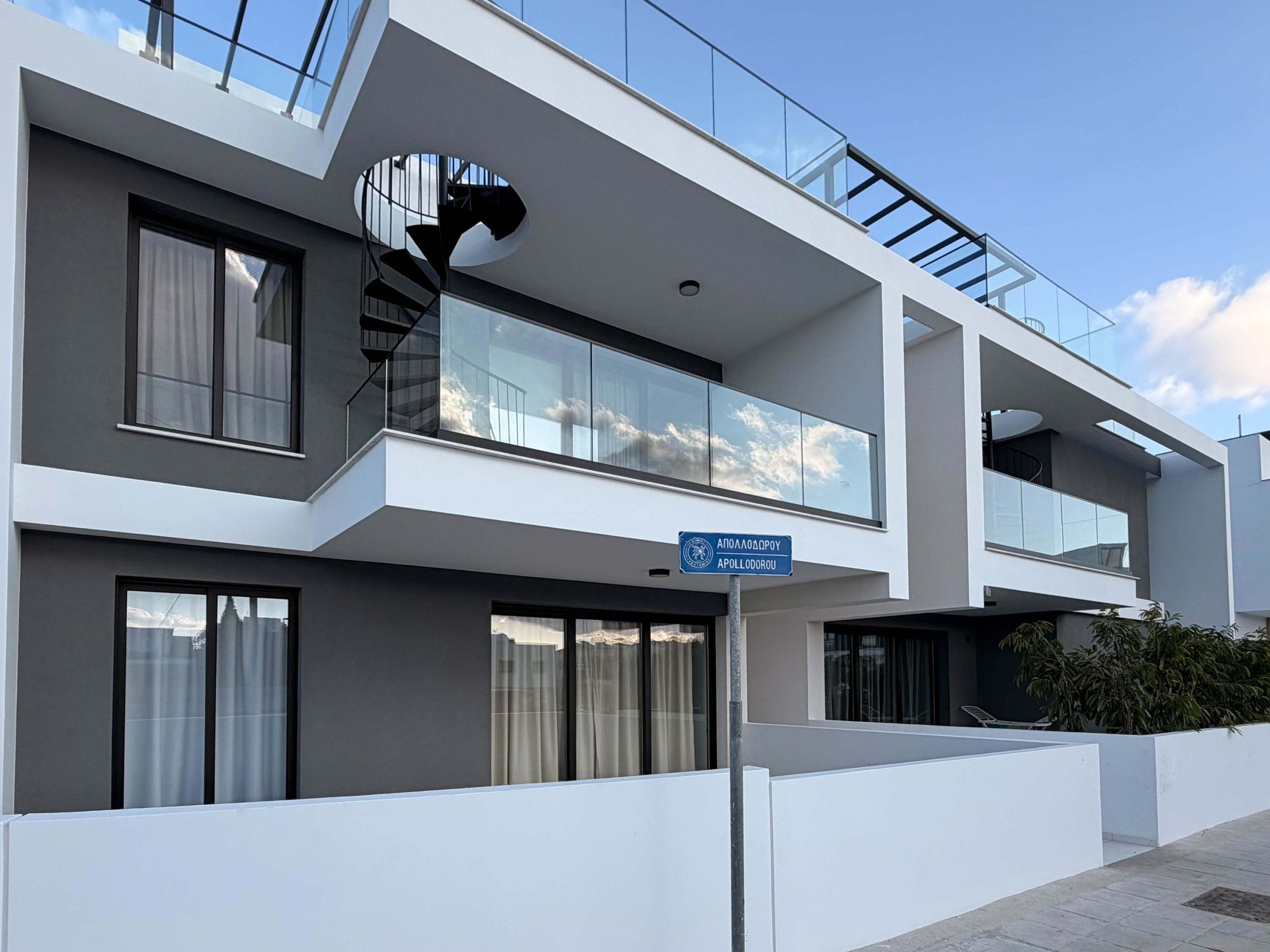 A modern multi-story building with a glass balcony, a spiral staircase, and a clear sky.