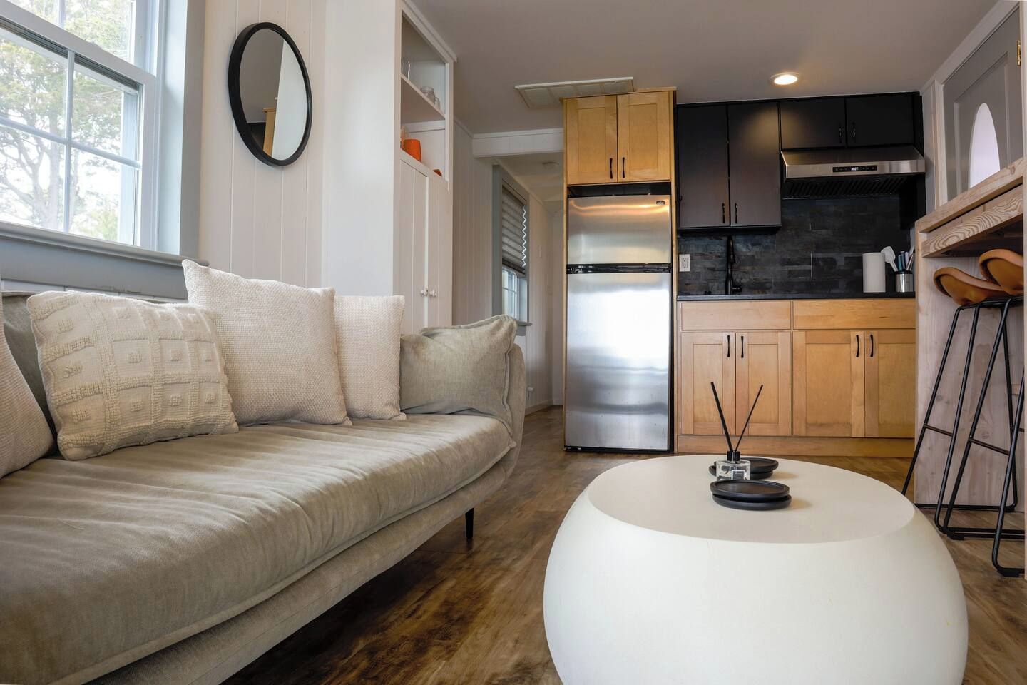 A modern living room with a sofa, a round coffee table, and a kitchen area with wooden cabinets and a stainless steel refrigerator.