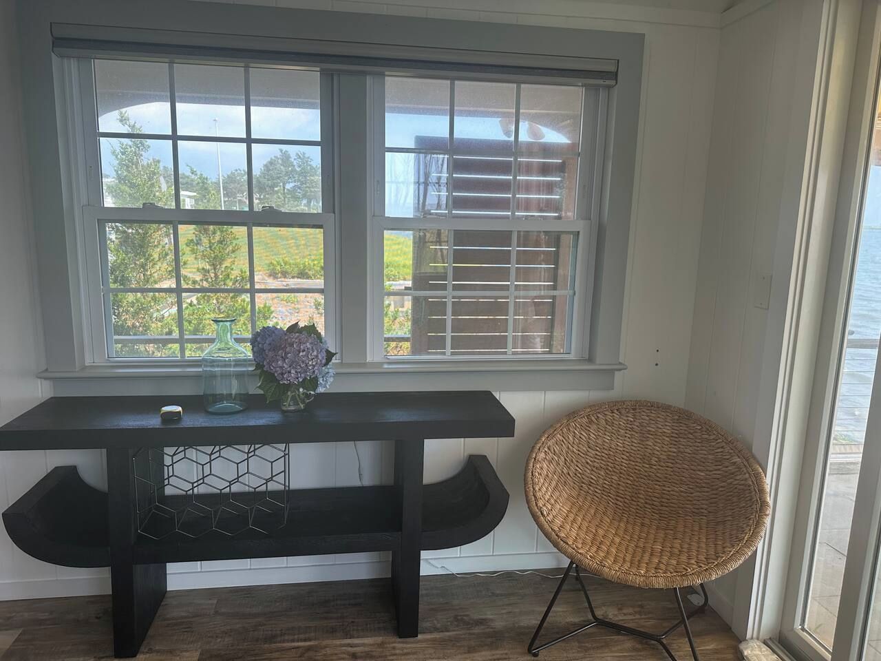 A room with a dark wooden table, a wicker chair, and a window with blinds.