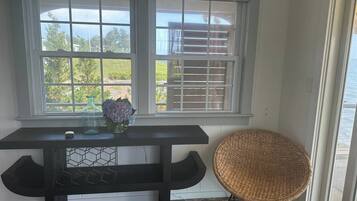 A room with a dark wooden table, a wicker chair, and a window with blinds.