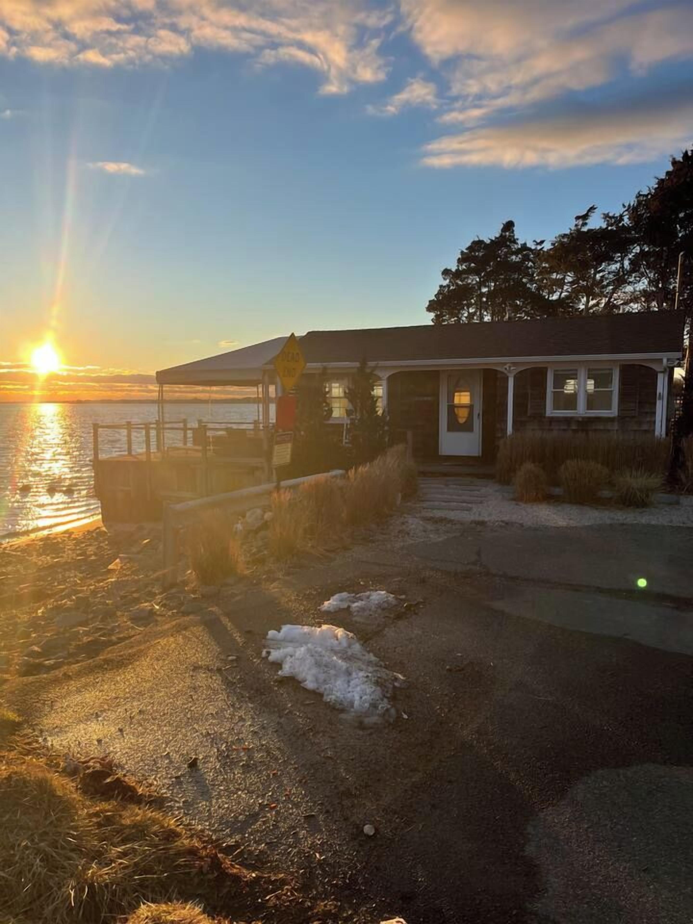 Ein Gebäude mit Veranda, einem Schild und Blick auf den Sonnenuntergang über dem Wasser.