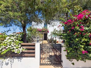 A gated entrance with a staircase leading to a building, surrounded by lush greenery and flowering plants. - Saint Elias Skyview | Hilltop Villa & Garden (Protaras)