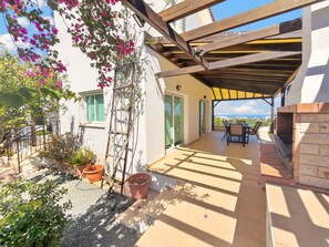 Eine überdachte Terrasse mit Tisch und Stühlen, einem Backofen aus Ziegeln und Blick auf die Landschaft.