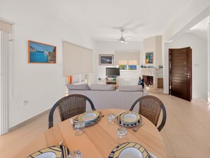 Un coin repas avec une table dressée pour quatre personnes, un téléviseur en arrière-plan et une cheminée.
