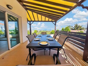 An outdoor dining area with a table set for four, surrounded by chairs, under a yellow pergola. - Saint Elias Skyview | Hilltop Villa & Garden (Protaras)
