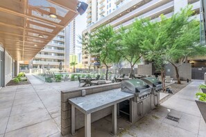 An outdoor patio with a grill station, seating area, and a pool in the background. - Sleek 2BR | Pool | W/D | Wi-Fi Near Arts District (Phoenix)