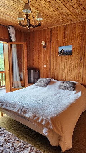 A wooden-paneled room with a bed, a picture on the wall, and a window with curtains. - Quiet 8-person chalet with a magnificent view of the mountains, fireplace,garden (Abondance)