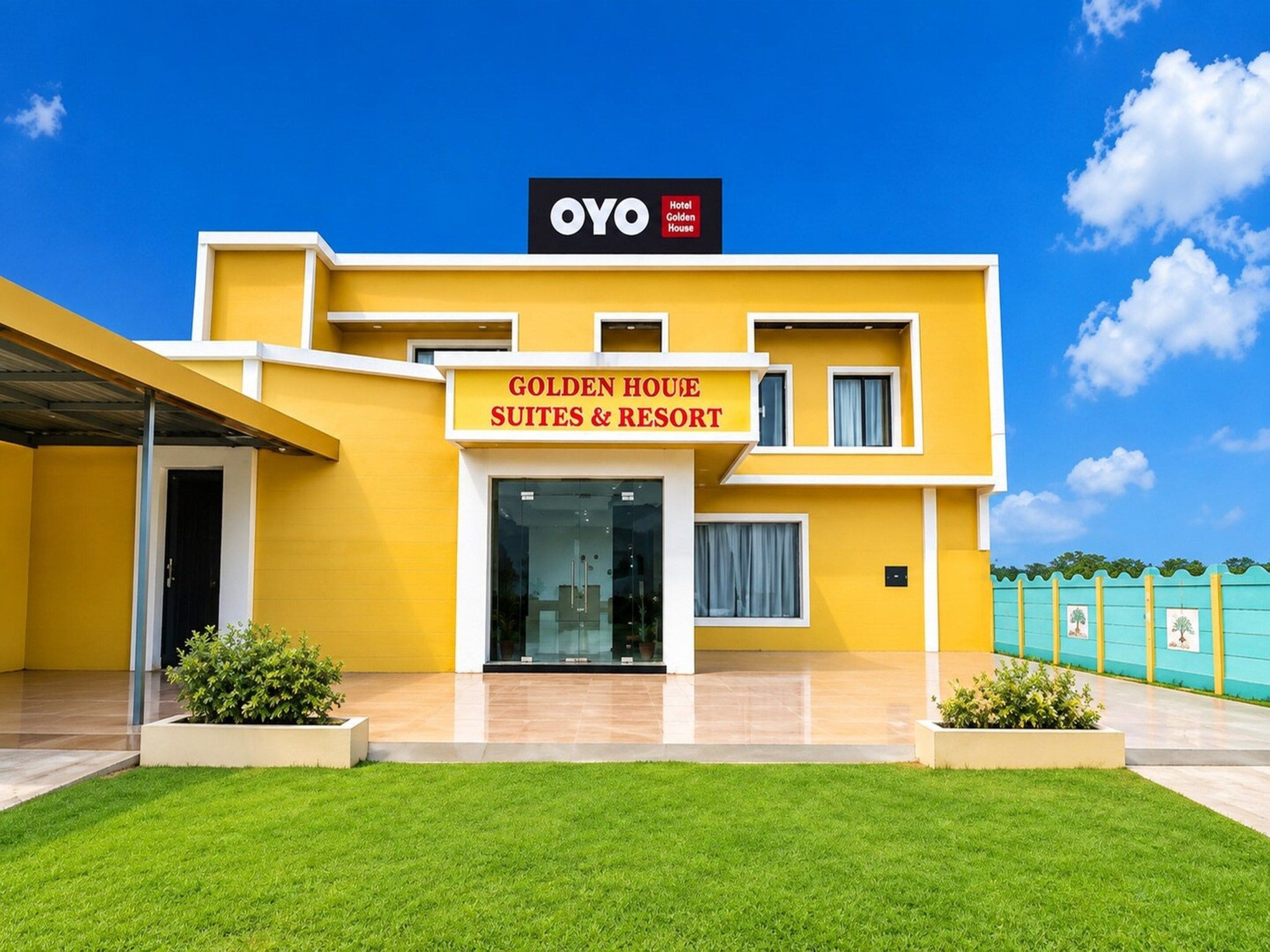 A modern hotel with a yellow facade, a sign for 'Golden House Suites & Resort,' and a clear blue sky.