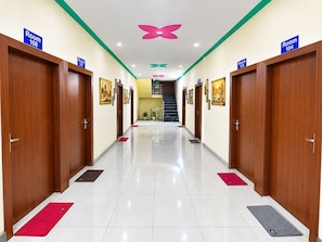 A hotel hallway with multiple doors labeled 'Room 108' and 'Room 104', a staircase, and a butterfly-shaped ceiling decoration. - Classic Golden Resort (Gohana)