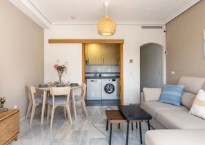 A modern living room with a sofa, a dining table with chairs, a kitchen area with a washing machine, and a hanging light fixture. - Penthouse with large private roof terrace - Calpe (Calp)