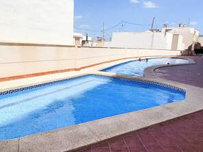 A swimming pool with a curved design, surrounded by a tiled deck and a white wall. - Penthouse with large private roof terrace - Calpe (Calp)