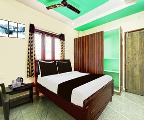 A hotel room with a bed, a desk with a kettle, a window with curtains, and a door. - Classic Akshaya Kannur (Penumuluru)
