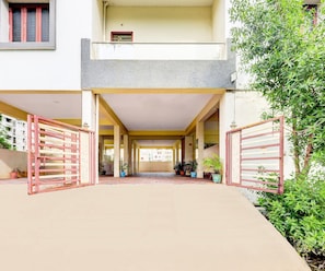 A building entrance with a covered walkway, potted plants, and a gated area. - Classic Akshaya Kannur (Penumuluru)