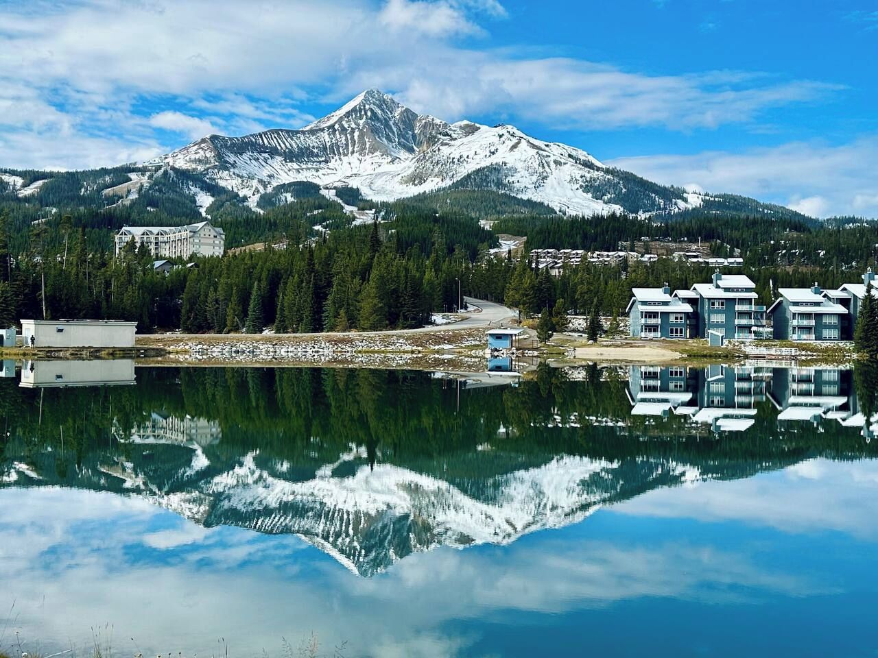 Una montaña con cima nevada, un cuerpo de agua que refleja la montaña, y edificios con diseño moderno.