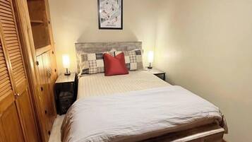 Une chambre à coucher avec un plafond en bois, un lit doté d’une tête de lit, deux tables de chevet et un luminaire fixé au mur.