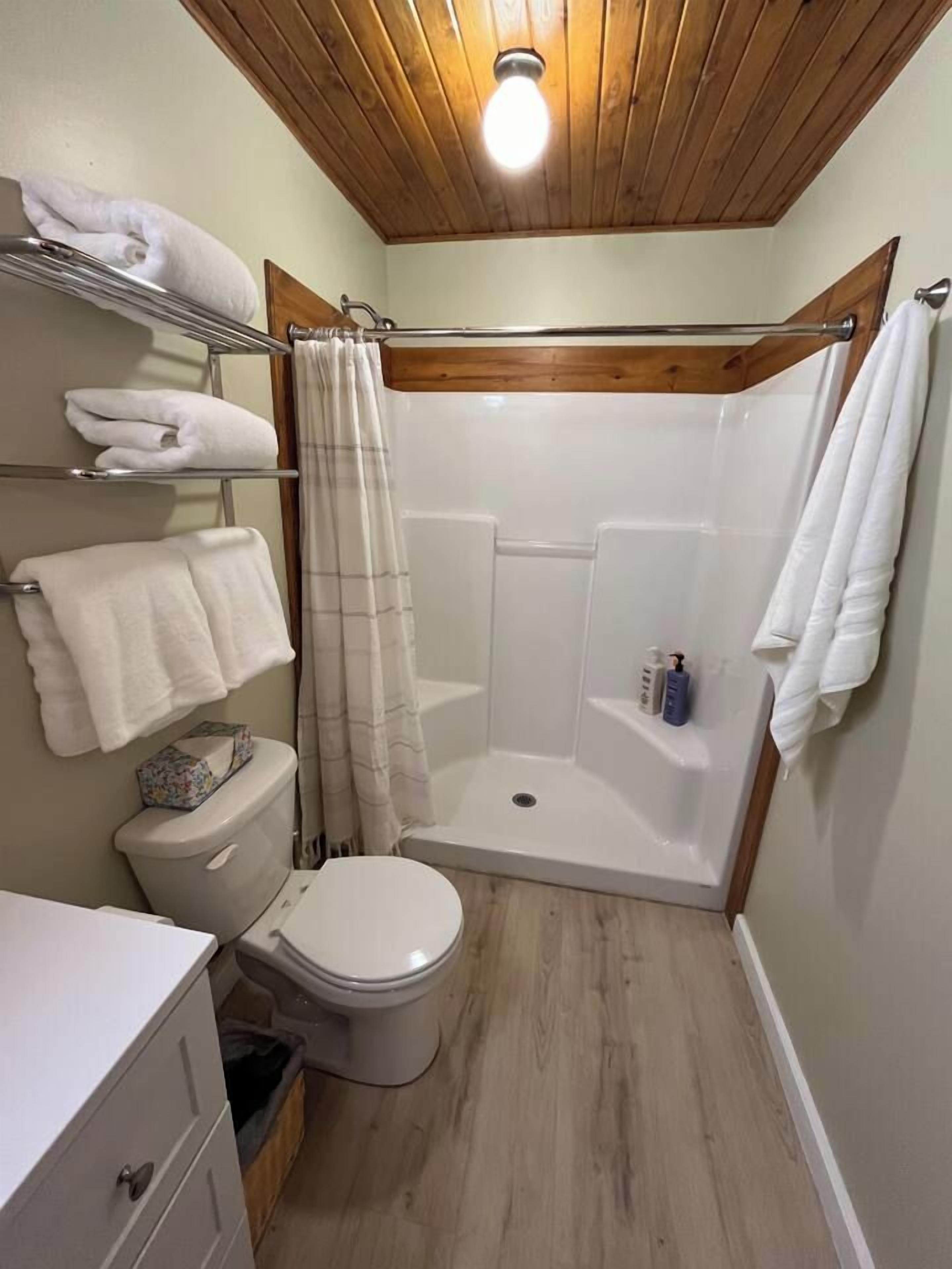 Een kleine badkamer met een douche, toilet en een plank met handdoeken.