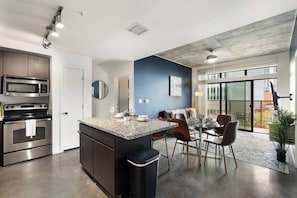 A modern kitchen with built-in appliances, a dining area with a glass table and chairs, and a large sliding glass door to the outside. - Trendy 2BR w/ Pool, W/D & Wi-Fi | Arts District (Phoenix)