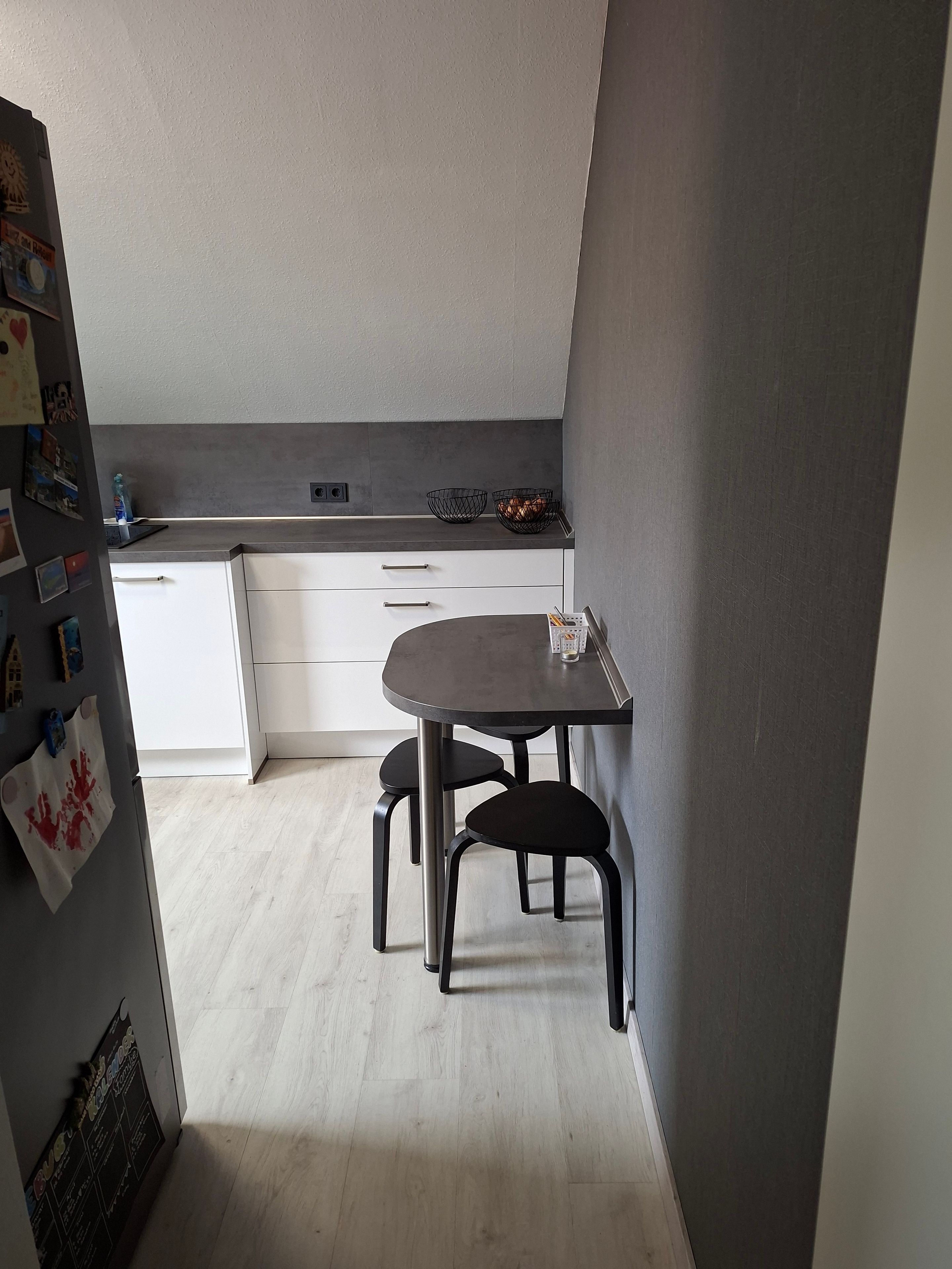 Eine kompakte Küche mit Essbereich, ausgestattet mit einem Tisch, zwei Stühlen, einer Arbeitsplatte mit einem Korb und einem Kühlschrank.
