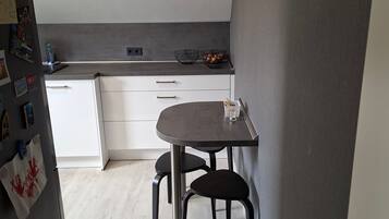 Eine kompakte Küche mit Essbereich, ausgestattet mit einem Tisch, zwei Stühlen, einer Arbeitsplatte mit einem Korb und einem Kühlschrank.