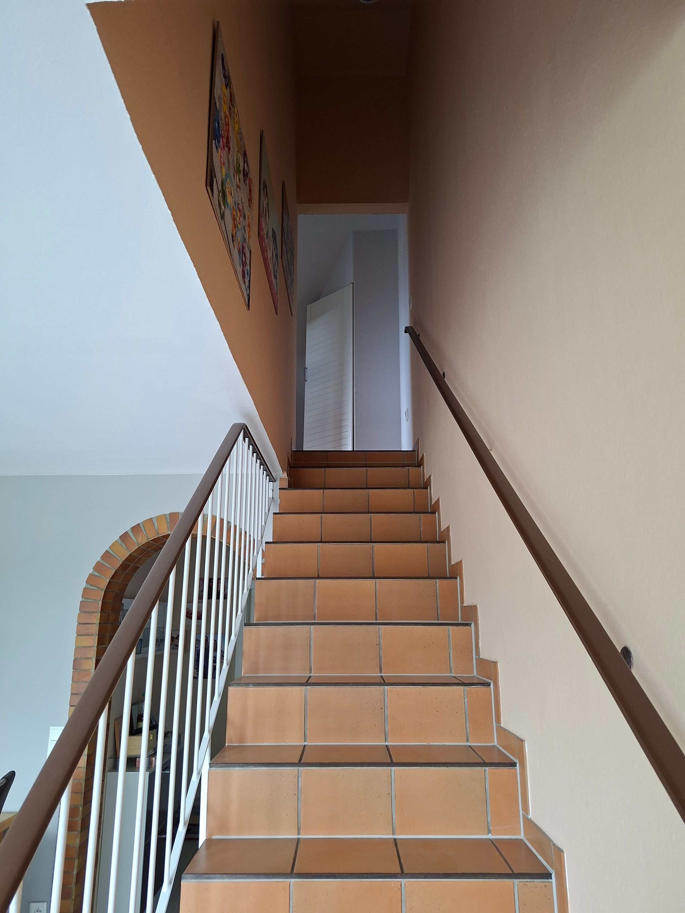 Una escalera con un muro de ladrillo a un lado y una barandilla blanca al otro, que conduce a una puerta en la parte superior.