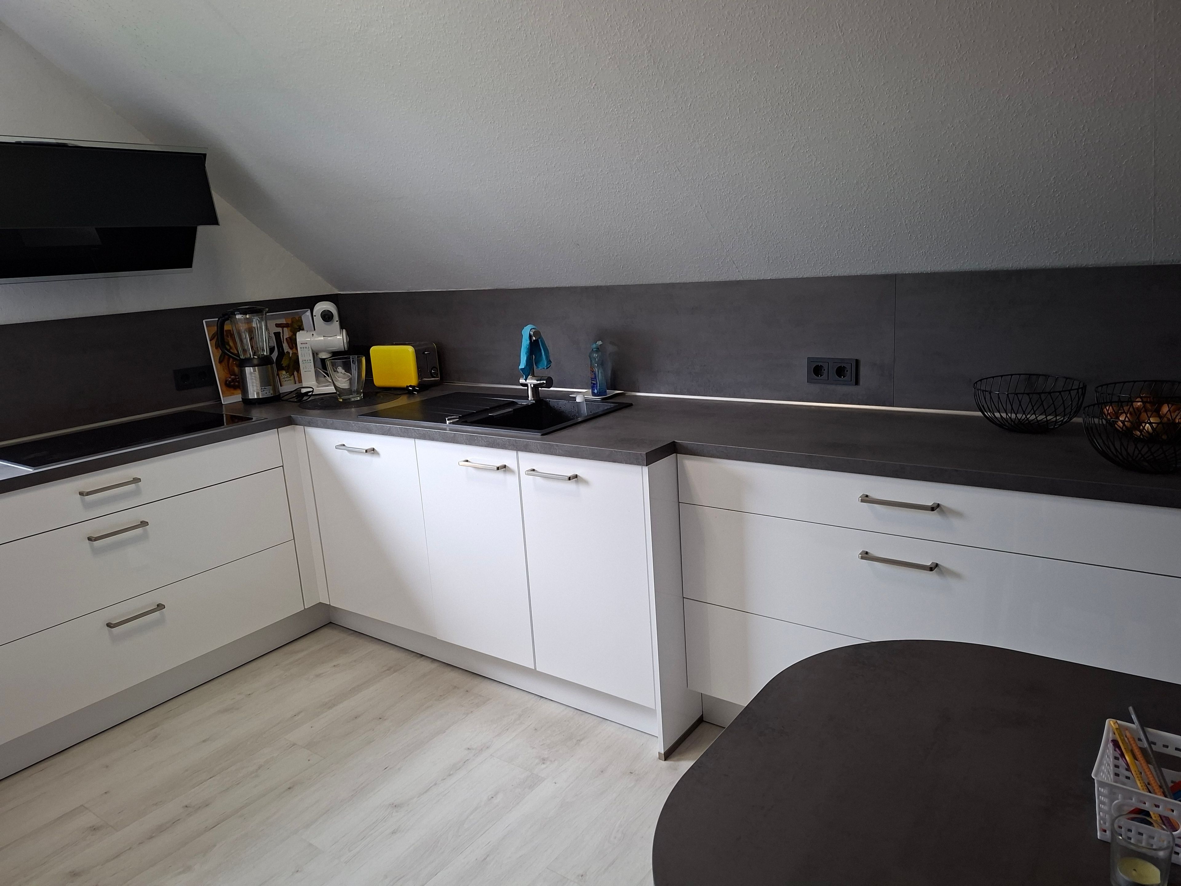 Eine moderne Küche mit weißen Schränken, einer grauen Arbeitsplatte und einer schwarzen Spritzschutzwand.