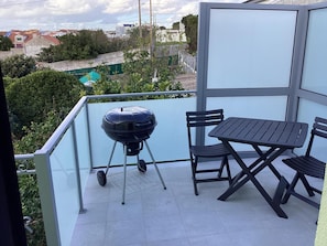 Ein Balkon mit Grill, Tisch und zwei Stühlen.