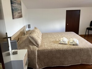 Un lit bien fait, avec une couvre-lit à motifs et des oreillers, une table de chevet avec une lampe, une porte et une chaise dans une pièce aux murs unis.