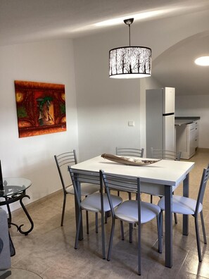 Un coin repas avec une table blanche, des chaises grises et un luminaire suspendu.