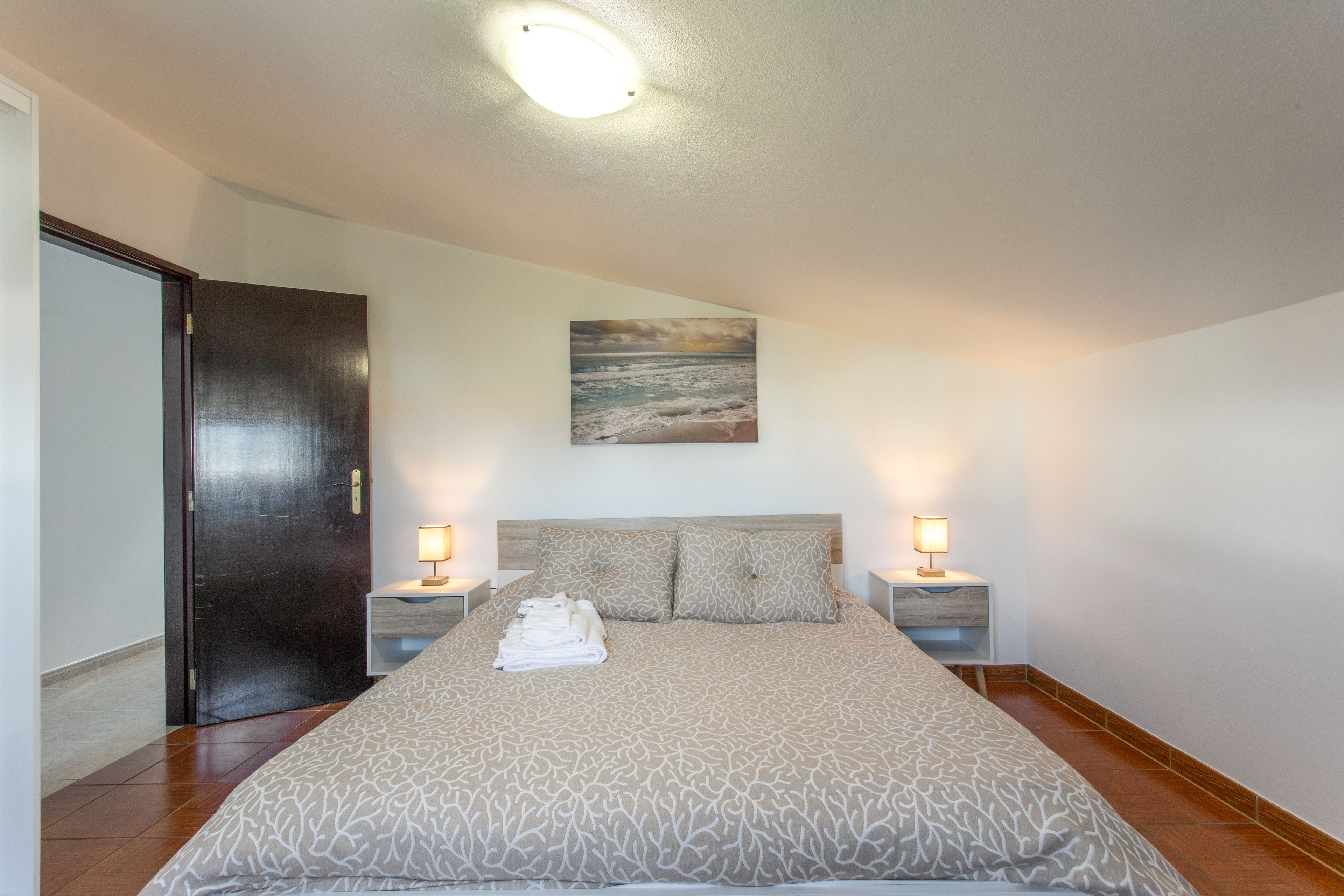 Un dormitorio con una cama, dos mesitas de noche, un cuadro en la pared y una puerta.