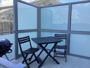 A balcony with a table and two chairs, a grill, and a view of the cityscape. - Apartment 'Vista Mar' with Sea View, Wi-Fi and Air Conditioning (Lourinhã)