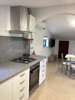 A kitchen with a gas stove, white cabinets, and a dining area with a table and chairs. - Apartment 'Vista Mar' with Sea View, Wi-Fi and Air Conditioning (Lourinhã)