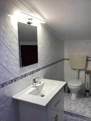 Une salle de bain avec un lavabo blanc, un miroir et des toilettes.