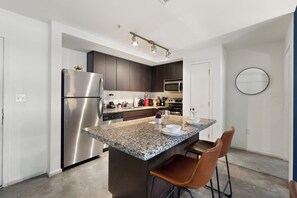 A modern kitchen with a stainless steel refrigerator, granite countertop, dark wooden cabinets, and a built-in microwave. - Stylish 2BR+ | Pool & W/D | Near Art District (Phoenix)