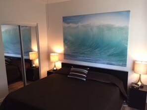 A hotel room with a bed, a large wall painting of a wave, and two bedside lamps. - Lakeview Ground-Floor Apartment (Chandler)