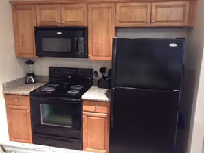 A kitchen with wooden cabinets, a black microwave, a black stove, and a black refrigerator. - Lakeview Ground-Floor Apartment (Chandler)