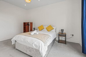 A bedroom with a bed, a bedside table with a lamp, a wardrobe, and a blue curtain. - Stylish 4BR Executive Home/Huge Kitchen/Sleeps7 (Bolton)